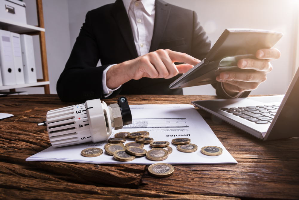 Businessperson's,Hand,Calculating,Invoice,With,Thermostat,And,Coins,On,Wooden